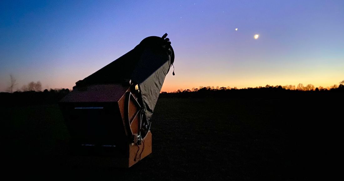 A Dobsonian pointing just over the horizon into a darkening sky as the light fades on the horizon